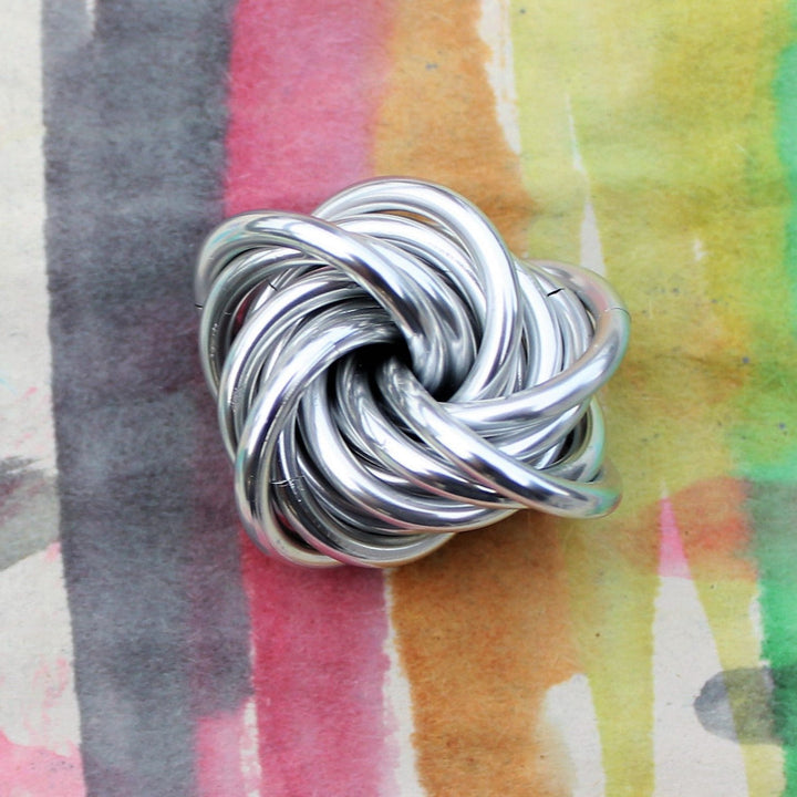 Silver stress fidget ball with twisted interlocking loop knot shape.