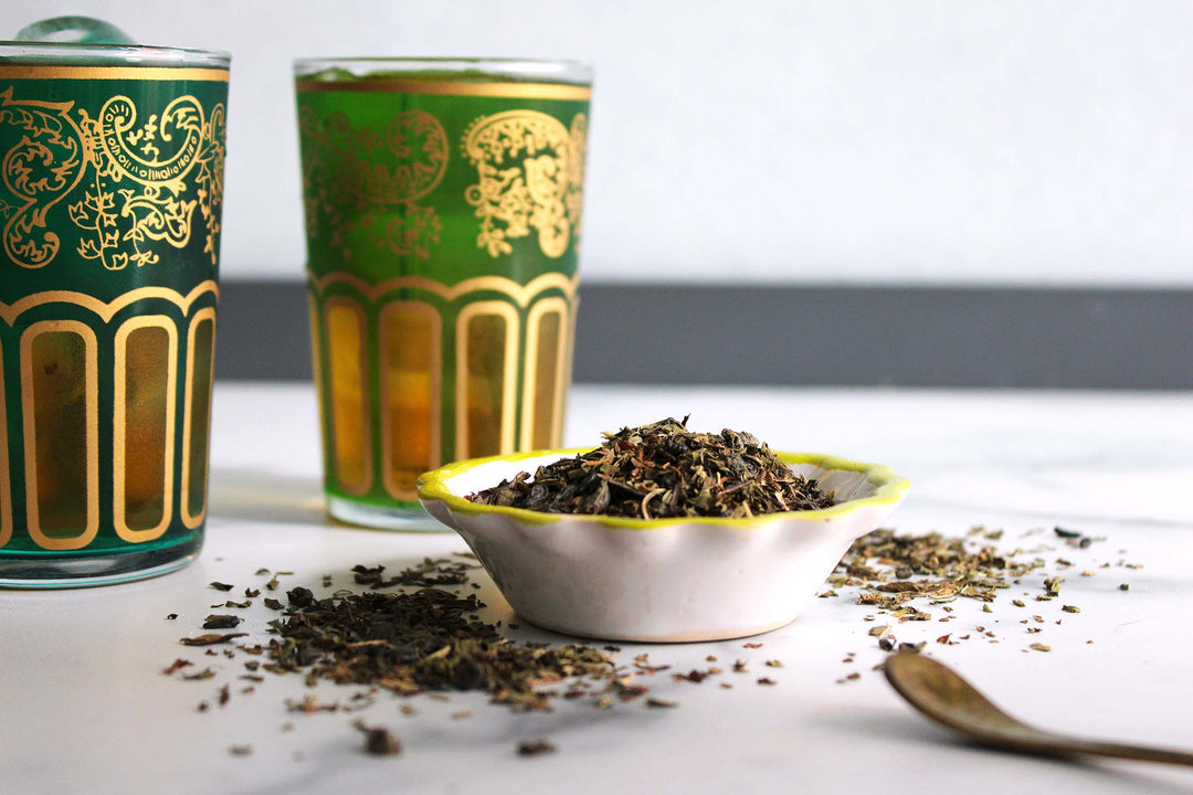 Small bowl of dried tea leaves with two decorative tins and a spoon.