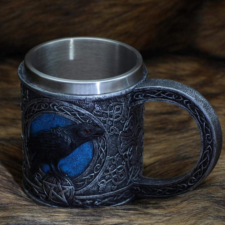 Stainless steel mug with raven-and-knot design, blue eye and markings, loop handle.