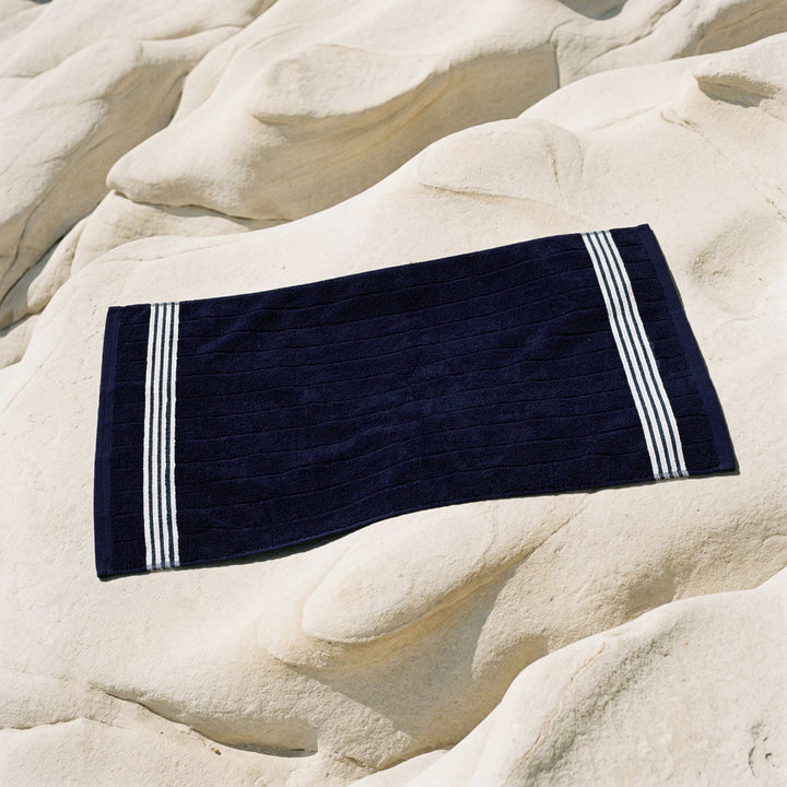 Folded navy cotton towel on a flat surface with white stripe border