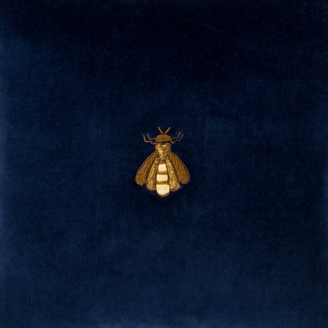 Close-up of navy velvet pillow cover with gold bee emblem embroidery