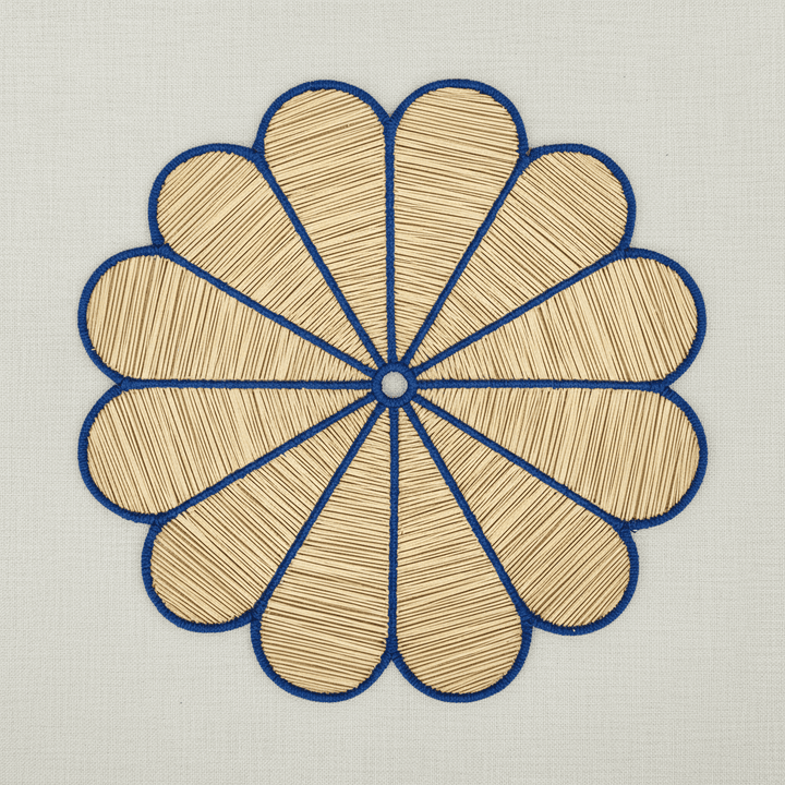 Handwoven iraca flower placemat with light pink-stitched petals and a natural woven center.