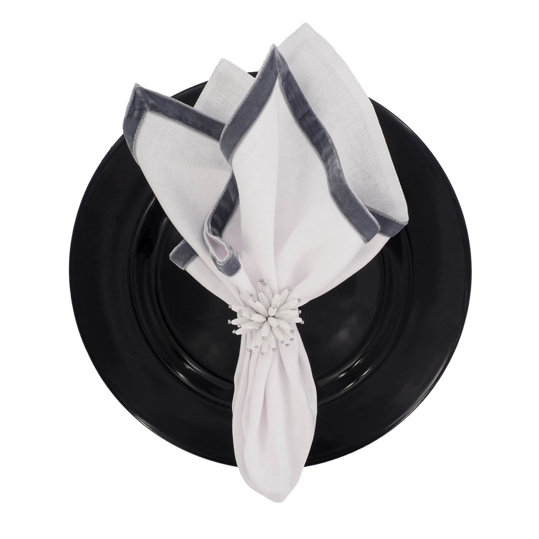 Linen napkins folded with dark velvet border, fastened with a white flower on a plate