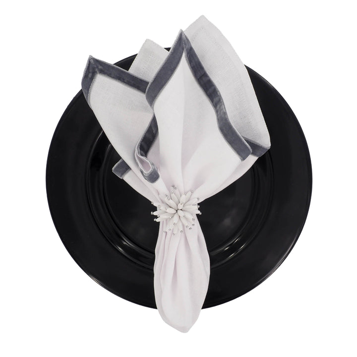Linen napkins folded with dark velvet border, fastened with a white flower on a plate