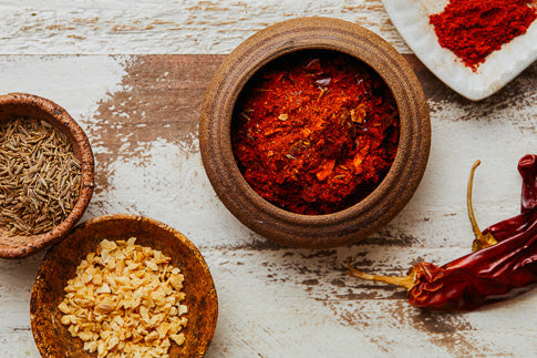 Red chili powder in a wooden bowl with dried chili peppers nearby.