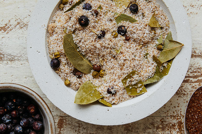 Brine seasoning mixture in bowl with bay leaves, peppercorns, and berries