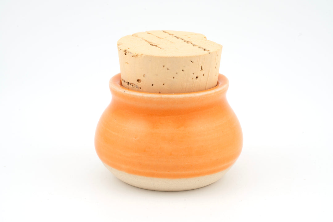 Mini corked jar with orange ceramic glaze and cork lid.