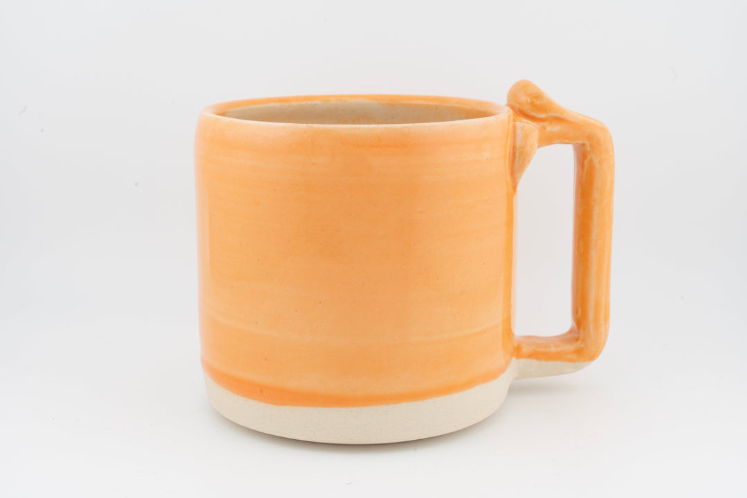 Ceramic mug with orange glaze, right-side handle, and creamy base