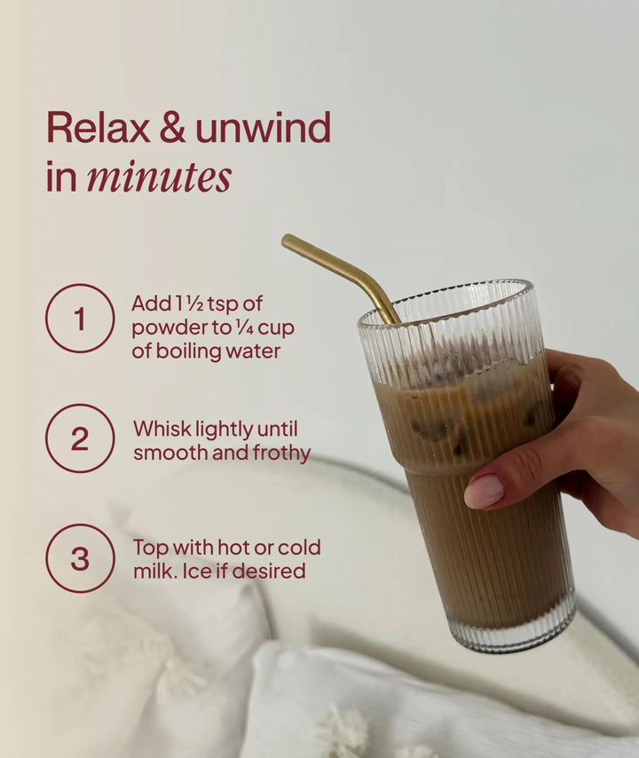 Hand holding a tall iced chai latte in clear glass with straw