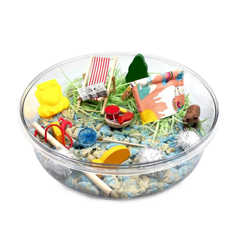 Clear round kinetic sand tray with green grass, tools, and beach-style sand pieces