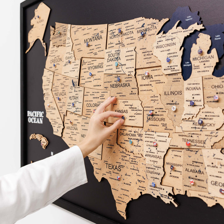 3D wooden USA map close-up with raised state pieces and small icons on black board