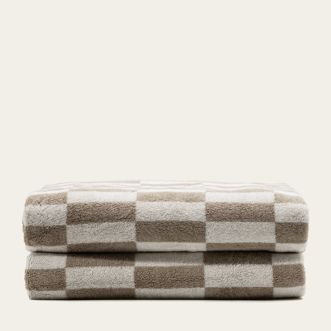 Folded tan and ecru checkered cotton bath towels, stacked in two layers