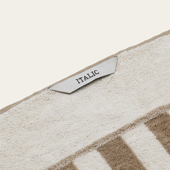 Cotton towel with beige-and-white texture and tag labeled “ITALIC”