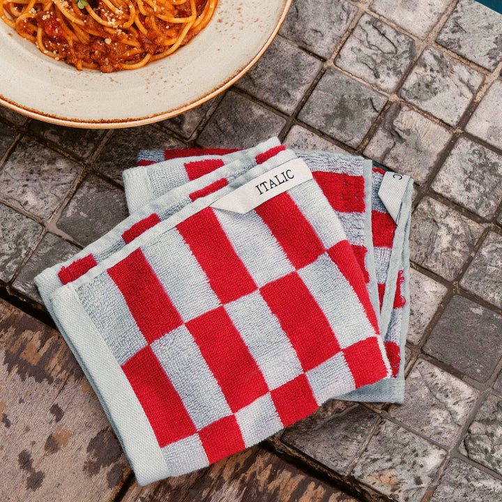 Red and white checkered cotton washcloths, folded set on gray stone surface.
