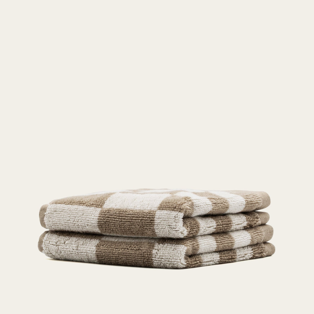 Folded tan and ecru checkered cotton bath towels, stacked neatly with rolled edges