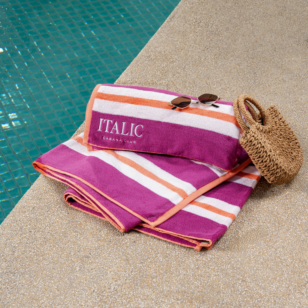 Cotton beach towel with purple and orange horizontal stripes, folded with sunglasses
