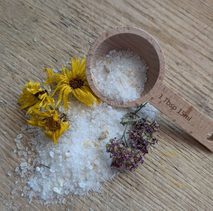 Lavender bath salt crystals in wooden scoop with dried flowers and 1 tbsp measure