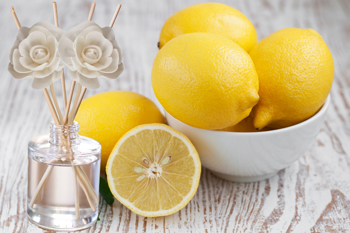 Reed diffuser bottle with rose topper beside lemons on a white bowl