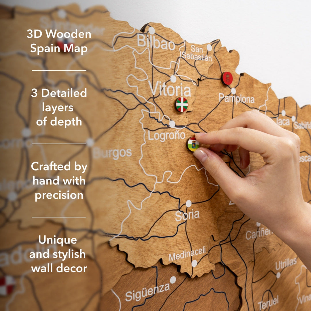 Oak wooden Spain map with layered 3D relief and a hand pressing a colored pin