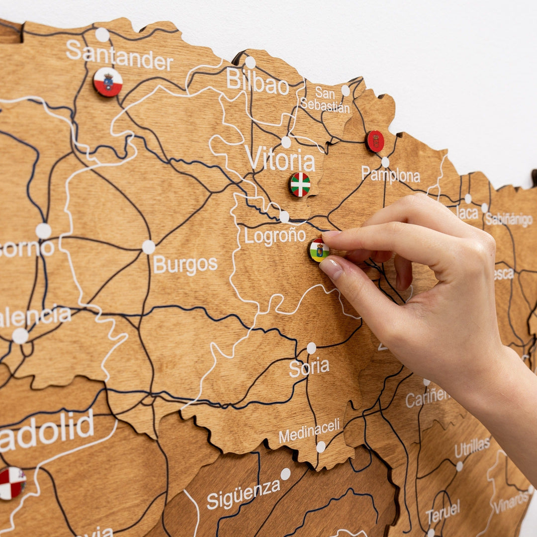 Oak wooden map of Spain with engraved roads and a hand placing a pin near Bilbao