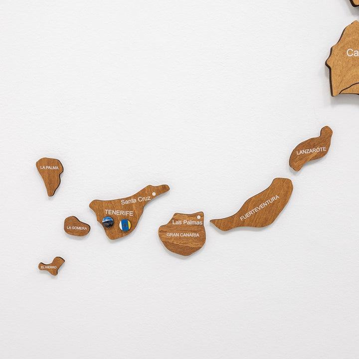 Wooden cutout islands of Spain with engraved names, arranged on a white wall