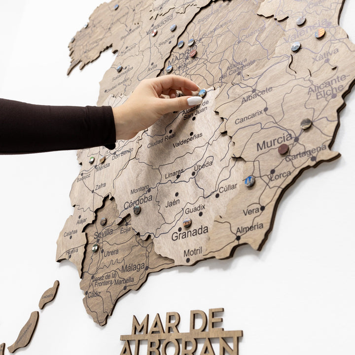 Wooden Spain map section with carved region names, push pins, and hand pointing