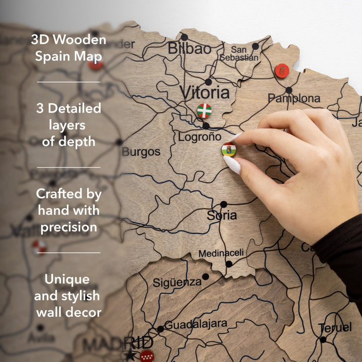 Layered wooden Spain map with engraved roads and region labels, hand pointing