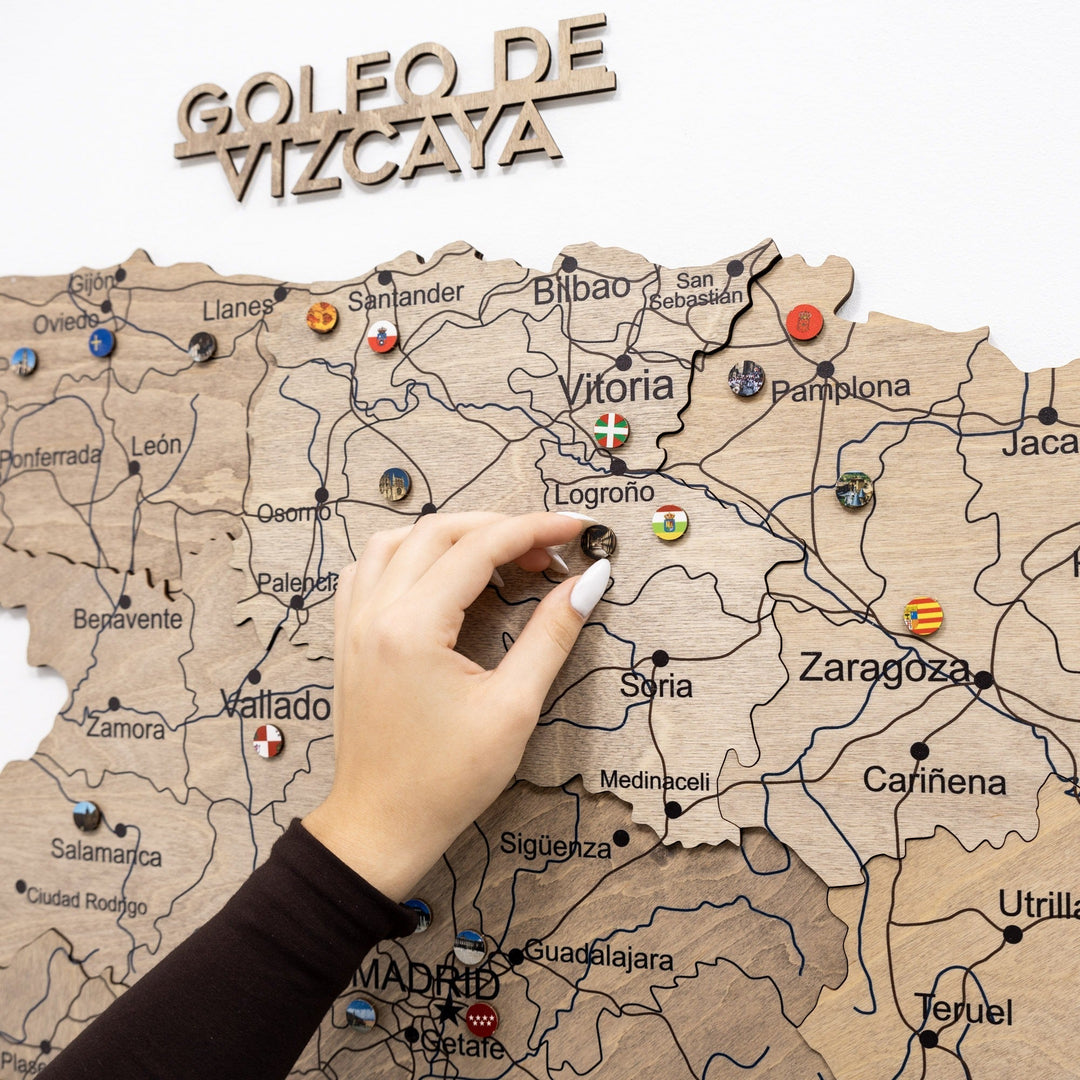 Wooden Spain map section with carved coast text and push pins, hand placing a pin