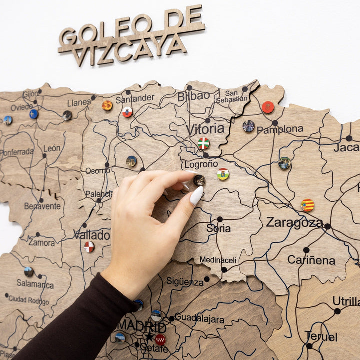 Wooden Spain map section with carved coast text and push pins, hand placing a pin