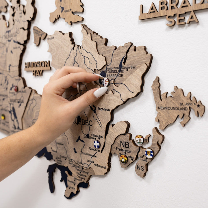 Close-up of wooden Canada map with Labrador Sea and NB pins and region outlines.