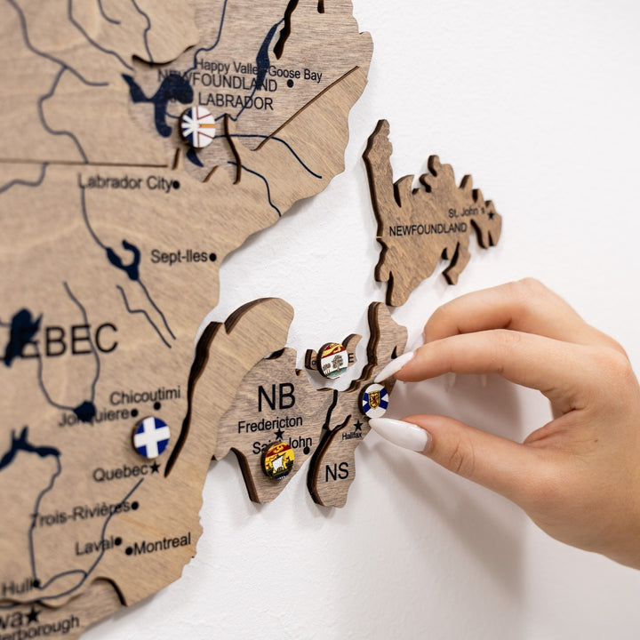 Close-up of wooden Canada map with souvenir pins for Newfoundland and Labrador, New Brunswick.