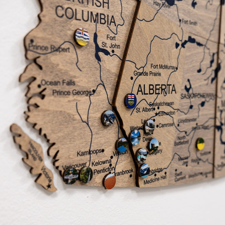 Close-up of wooden Canada map featuring British Columbia and Alberta with small souvenir pins.