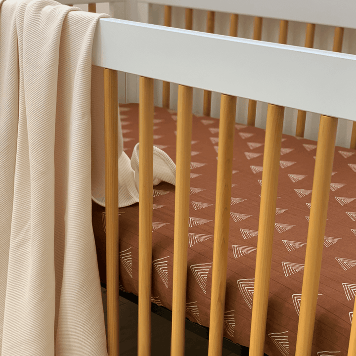 Fitted crib sheet in cream striped muslin fabric, tailored wraparound edges