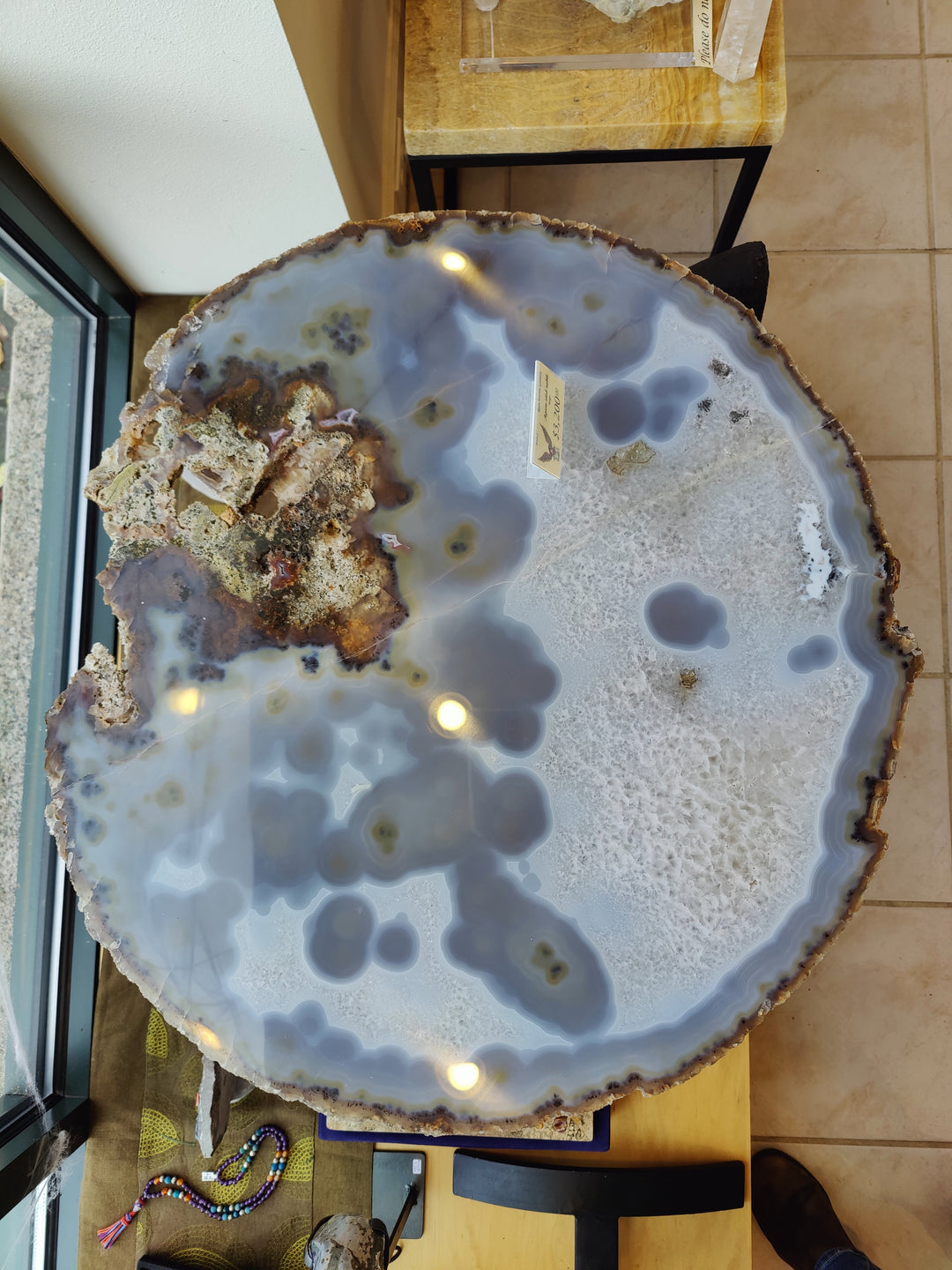 Round agate quartz slab with pale blue-gray surface, dark gray geode spots, rough rim