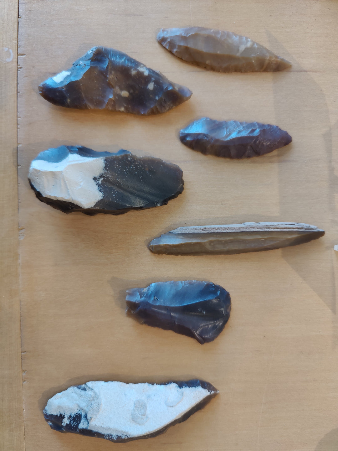 Assorted chipped blue and dark stone tools, arrowhead-shaped pieces