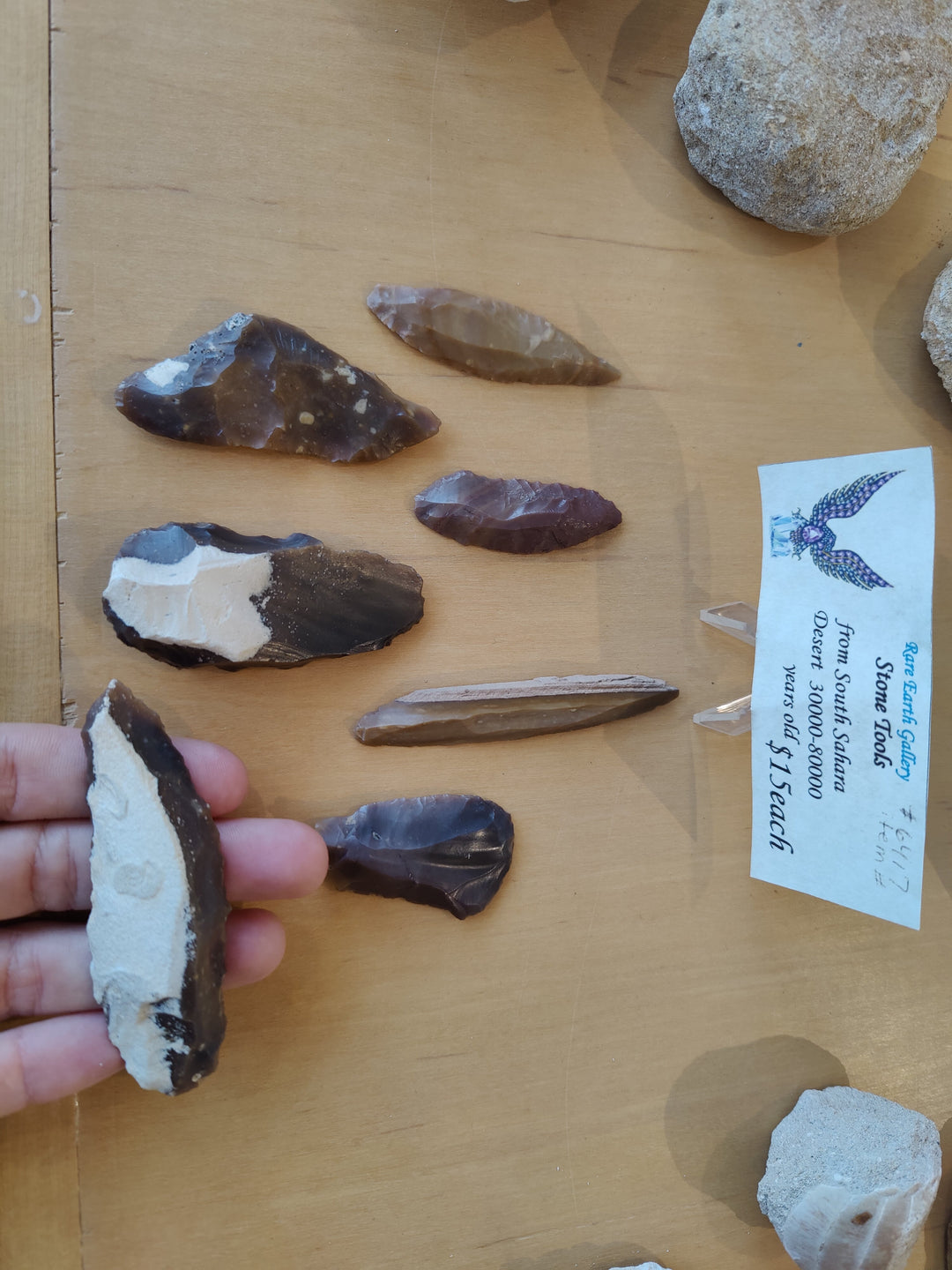 Hand holding a chipped stone tool with pointed edge; assorted stones on board