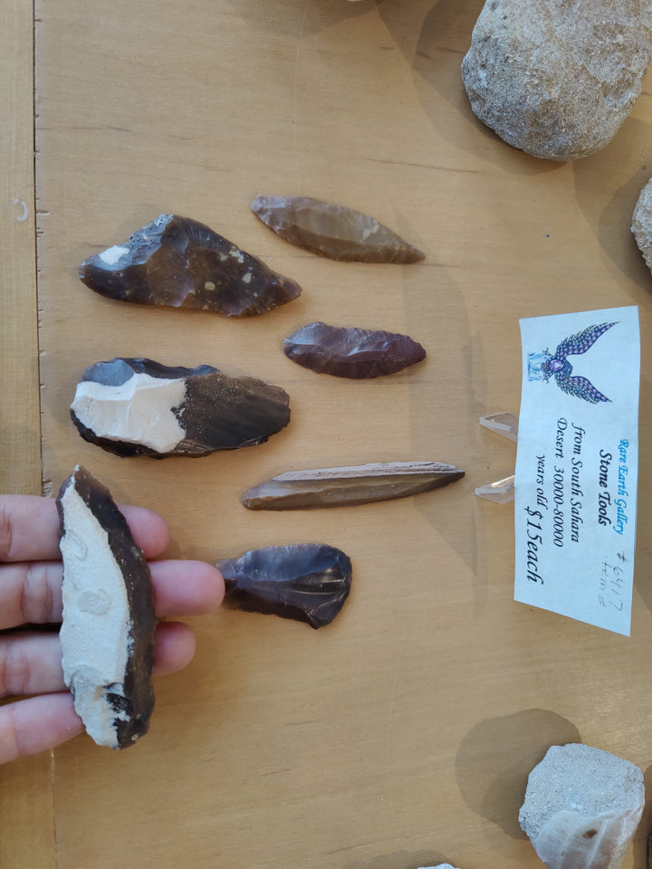 Hand holding a chipped stone tool with pointed edge; assorted stones on board