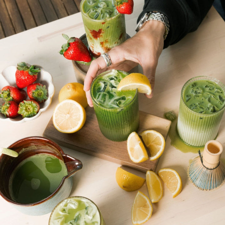 Single-cultivar matcha drinks and fresh tea leaves on a table, one being poured