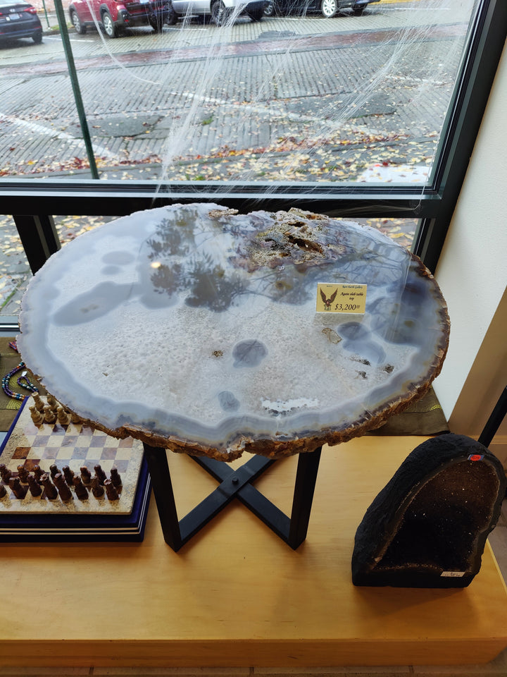 Large agate quartz slab with pale blue-gray pools and rough brown edge on X-stand