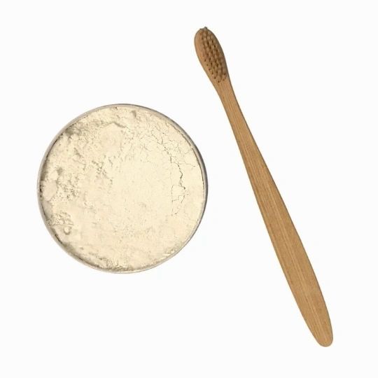 Tooth powder dish with pale beige powder and wooden scoop