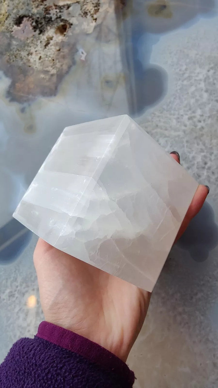 Selenite standing cube held in hand, translucent white facets.