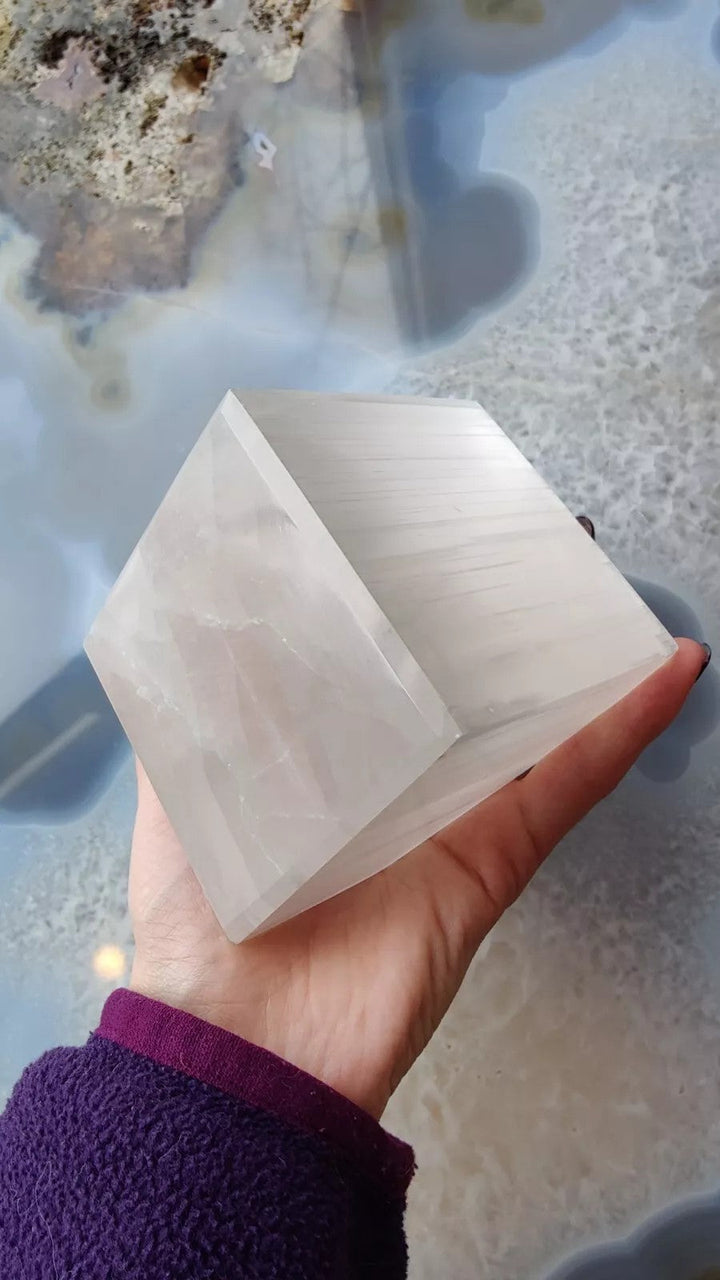 Translucent selenite cube with stepped facets, held in hand.