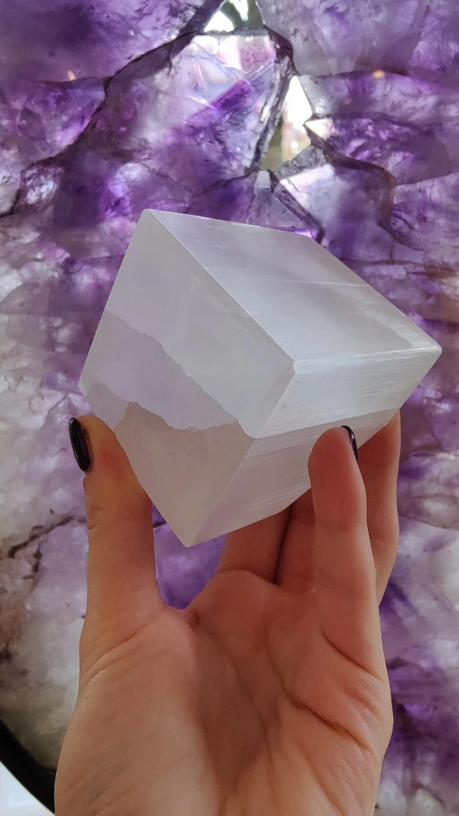 White selenite standing cube, translucent with sharp beveled edges, held in hand