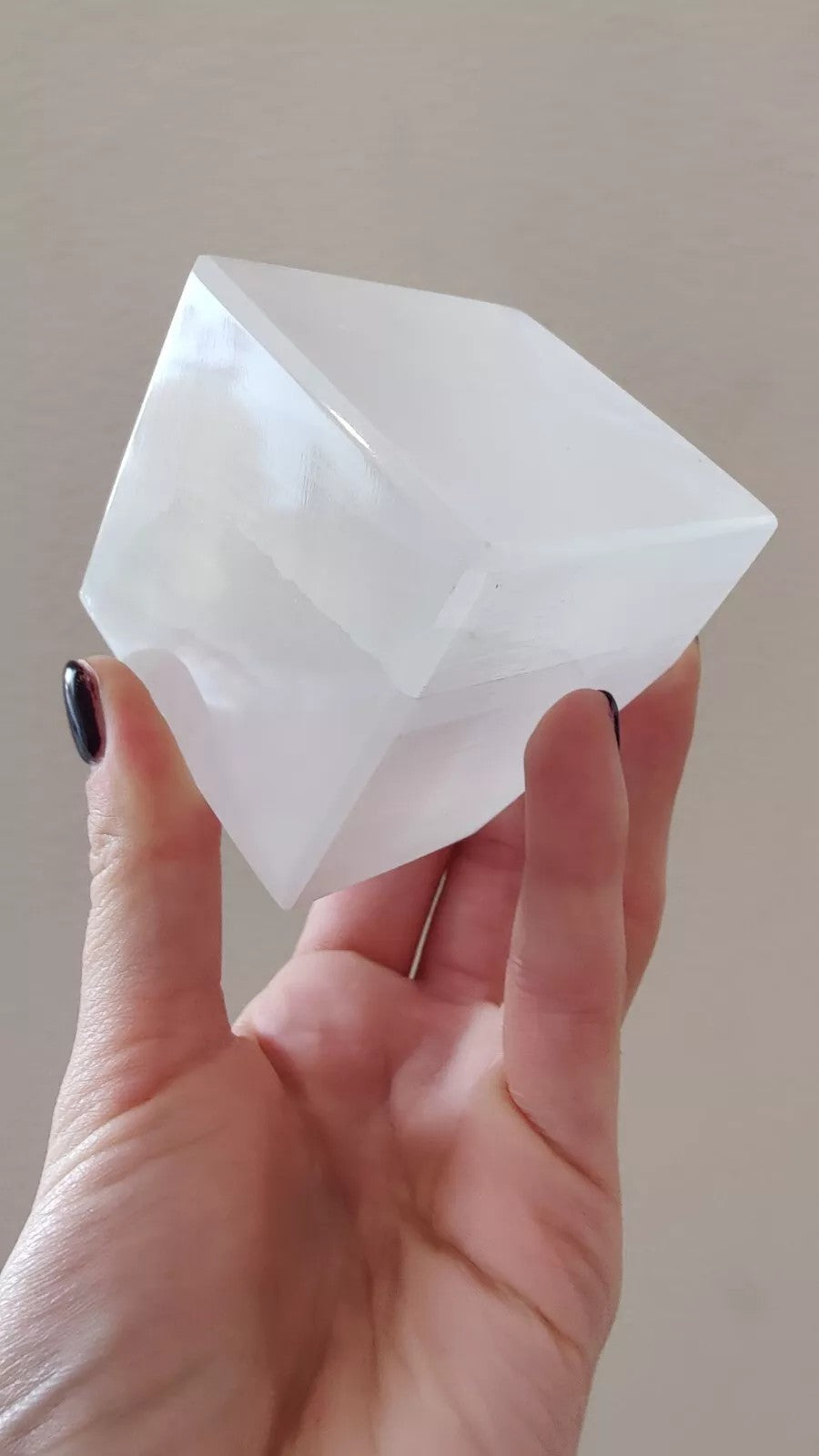 Translucent selenite cube with beveled corners, held up for a front view
