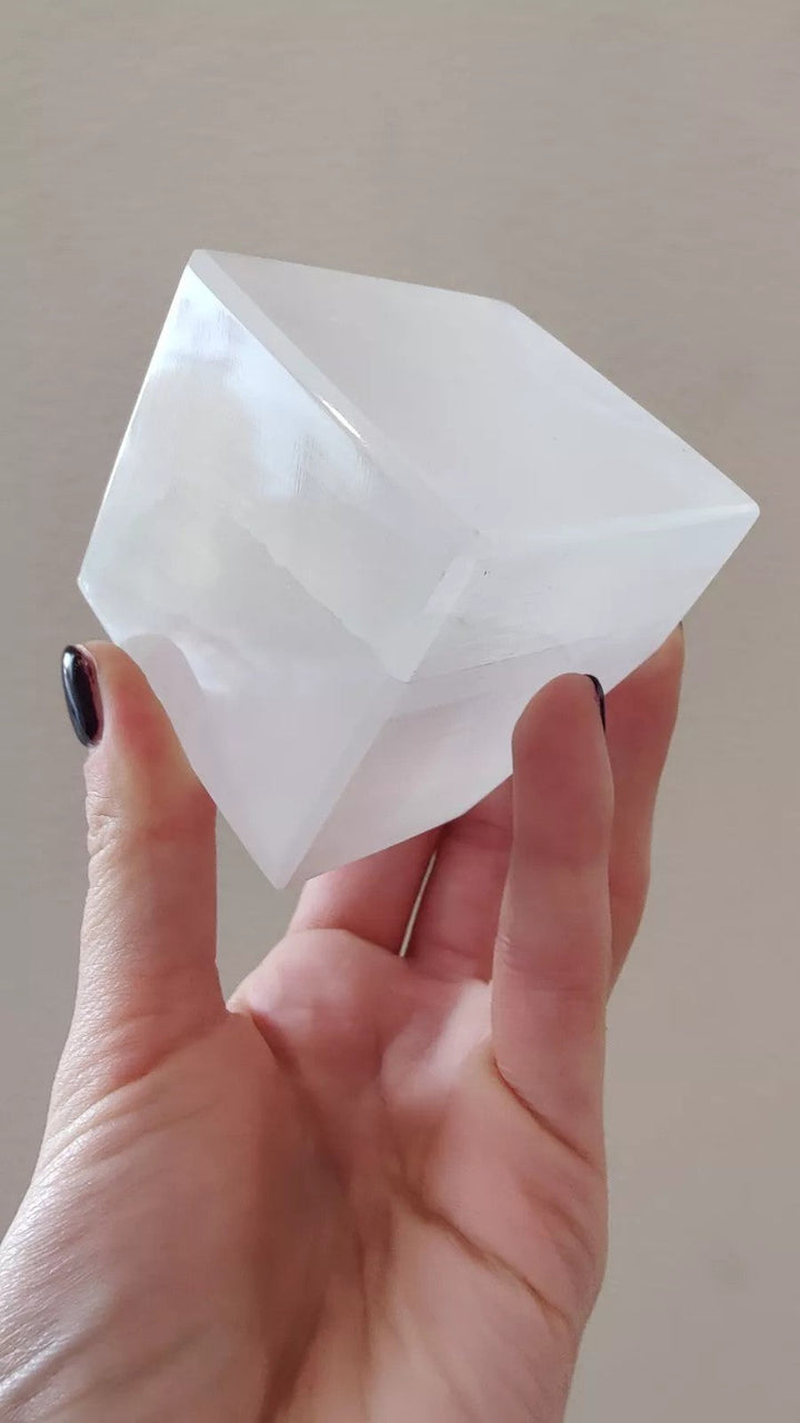 Translucent selenite cube with beveled corners, held up for a front view