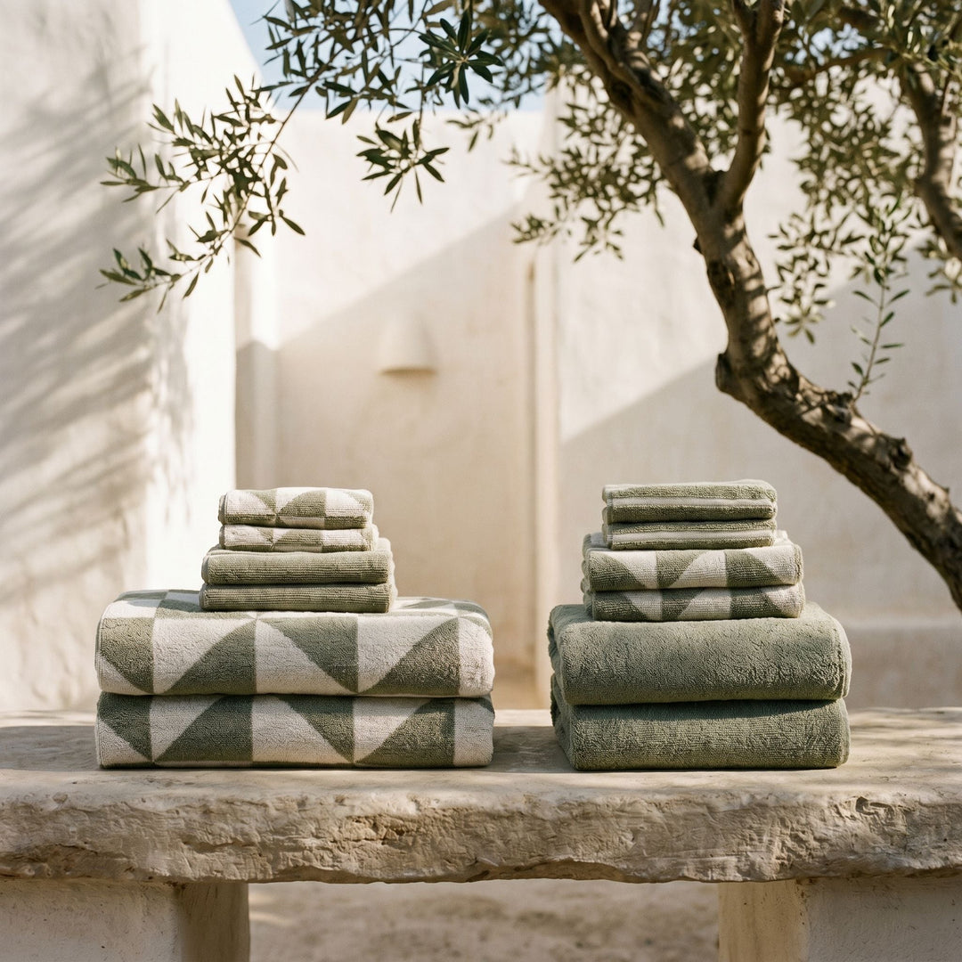 Folded sage-green cotton towels with geometric pattern and smooth borders.