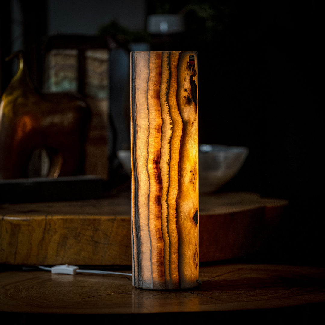 Tall cylinder table lamp with vertical amber onyx stripes and warm interior light.