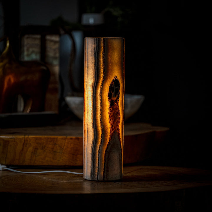 Cylinder table lamp with glowing amber onyx-patterned stone shade and dark base.