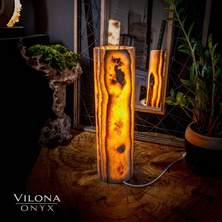 Tall onyx cylinder table lamp with dark mottled areas and bright amber glow through.