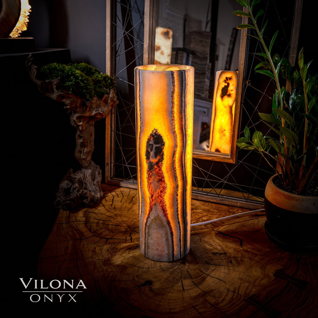 Onyx cylinder table lamp with open top and warm amber glow through the stone body.